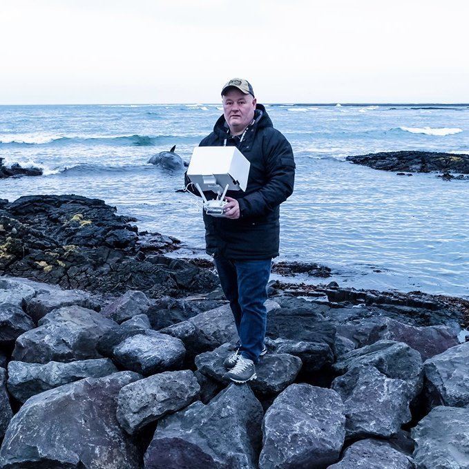 Jón Steinar að störfum. Með drónafjarstýringuna og búrhvalinn sem strandaði við Grindavík í baksýn.